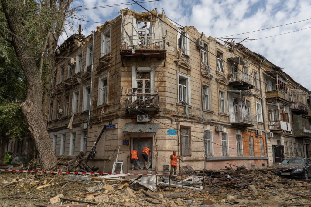 Communal workers clean debris next to a damaged residential building