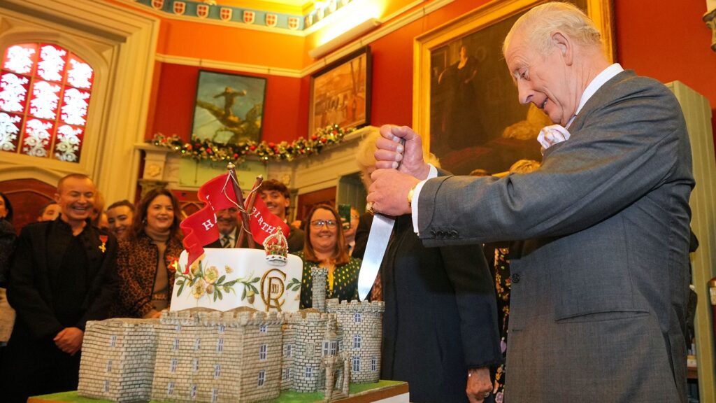 Britain’s King Charles III cuts into a castle-style cake as he and Britain’s Queen Camilla attend a celebratory reception to mark the 200th anniversary of Cyfarthfa Castle during a visit to the South Wales town of Merthyr Tydfil on November 14, 2025, on the King’s 77th birthday.